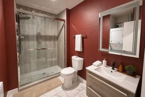A modern bathroom with a glass-enclosed shower, a white toilet, and a vanity with a mirror. - Moody Designer Retreat Near Greenville & Downtown (Dallas)