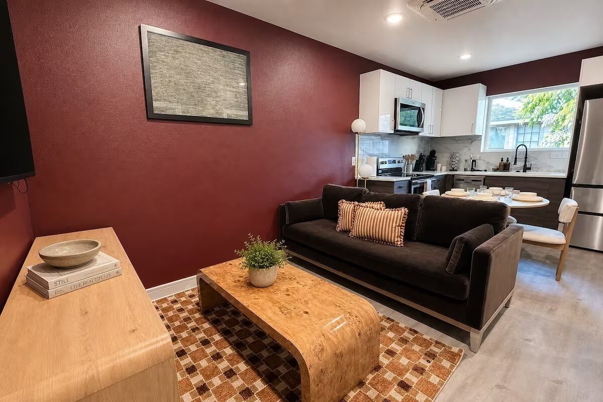 A modern living room with a dark sofa, a wooden coffee table, and a kitchen area in the background.