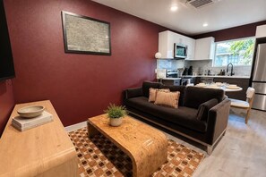 Un salon moderne avec un canapé foncé, une table basse en bois et un coin cuisine à l’arrière-plan.