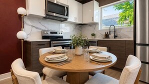 A modern kitchen with a marble backsplash, stainless steel appliances, and a dining area with a round table and chairs. - Moody Designer Retreat Near Greenville & Downtown (Dallas)
