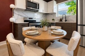 A modern kitchen with a marble backsplash, stainless steel appliances, and a dining area with a round table and chairs. - Moody Designer Retreat Near Greenville & Downtown (Dallas)
