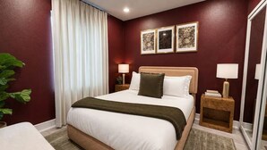 A hotel room with a large bed, two bedside tables with lamps, a window with curtains, and a plant. - Moody Designer Retreat Near Greenville & Downtown (Dallas)