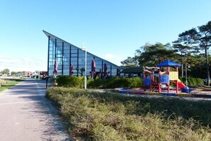A modern building with a glass facade, a playground with slides and climbing structures, and a clear sky. - Holiday apartment 2 in the Strandglück house (Glowe)