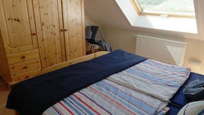 Quarto com claraboia, cama com roupa de cama listrada, guarda-roupa de madeira e radiador.