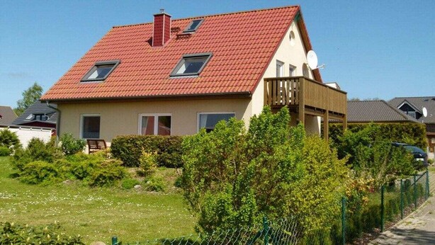 Uma casa de dois andares com telhado de telhas vermelhas, antena parabólica e quintal cercado.