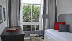 Un dormitorio con cama, mesita de noche, lámpara, ventana con cortinas y radiador.
