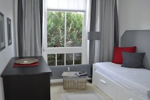 Un dormitorio con cama, mesita de noche, lámpara, ventana con cortinas y radiador.