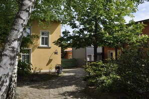 Ein Kopfsteinpflasterweg führt zu einem gelben Gebäude, vor dem ein Fahrrad steht.