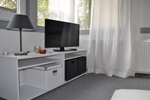 Ein Zimmer mit weißem Schreibtisch, Flachbildfernseher, Lampe und Heizkörper.