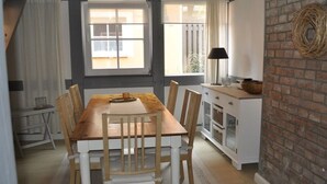 Un comedor con una mesa y sillas de madera, un armario blanco con puertas de cristal y una pared de ladrillo decorada con un adorno tejido.