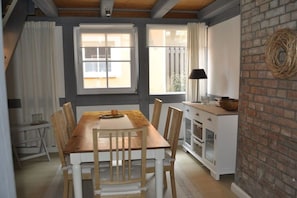 Un comedor con una mesa y sillas de madera, un armario blanco con puertas de cristal y una pared de ladrillo decorada con un adorno tejido.