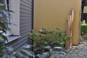 Eine Terrassenfläche mit einem Blumentopf, einem kleinen Tisch mit Tassen und an eine Wand gelehnten Holzbrettern.