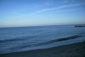 Ein Strand mit ruhigem Wasser, einem klaren Himmel und einem Holzsteg, der ins Meer führt.