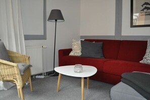Ein Wohnzimmer mit einem roten Sofa, einem weißen Couchtisch, einer Stehlampe und einem Korbstuhl.
