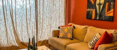 A living room with a sofa, a coffee table, a cactus plant, and a painting on the wall.