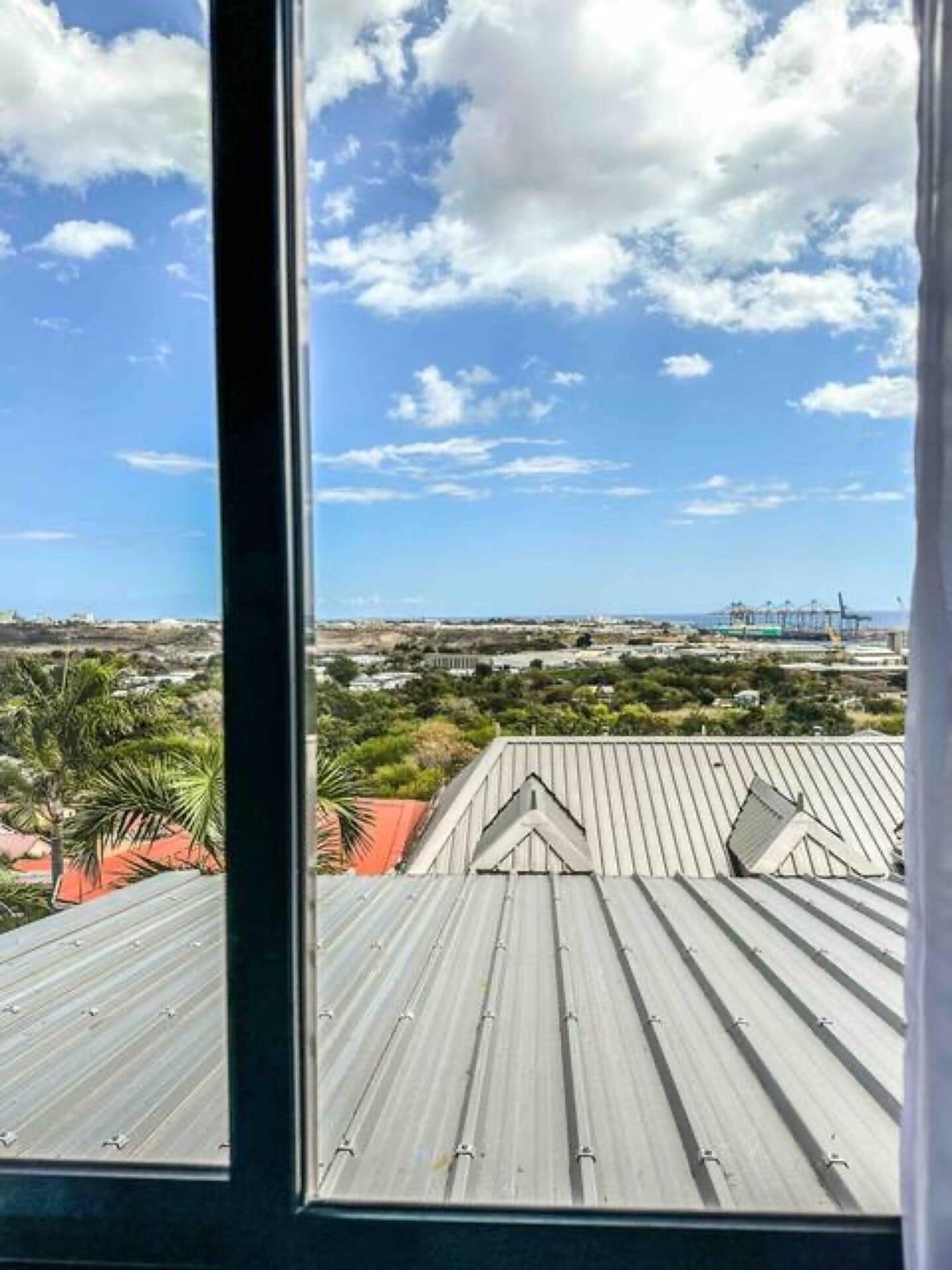 Vista desde una ventana sobre un paisaje urbano con cielo despejado y algunas nubes dispersas.