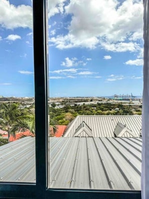 A view from a window overlooking a cityscape with a clear sky and scattered clouds. - The Getaway (La Possession)
