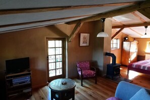 A cozy room with a television, a chair, a table, a bed, and a wood-burning stove. - "Zur Tenne" - in the Müritz National Park (Mirow\/OT Babke)