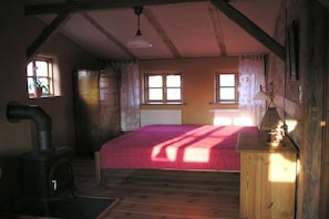 A room with a bed, a wooden dresser, a stove, and two windows. - "Zur Tenne" - in the Müritz National Park (Mirow\/OT Babke)