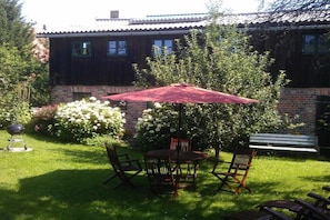 A patio with a table and chairs, a red umbrella, and a brick wall in the background. - "Zur Tenne" - in the Müritz National Park (Mirow\/OT Babke)