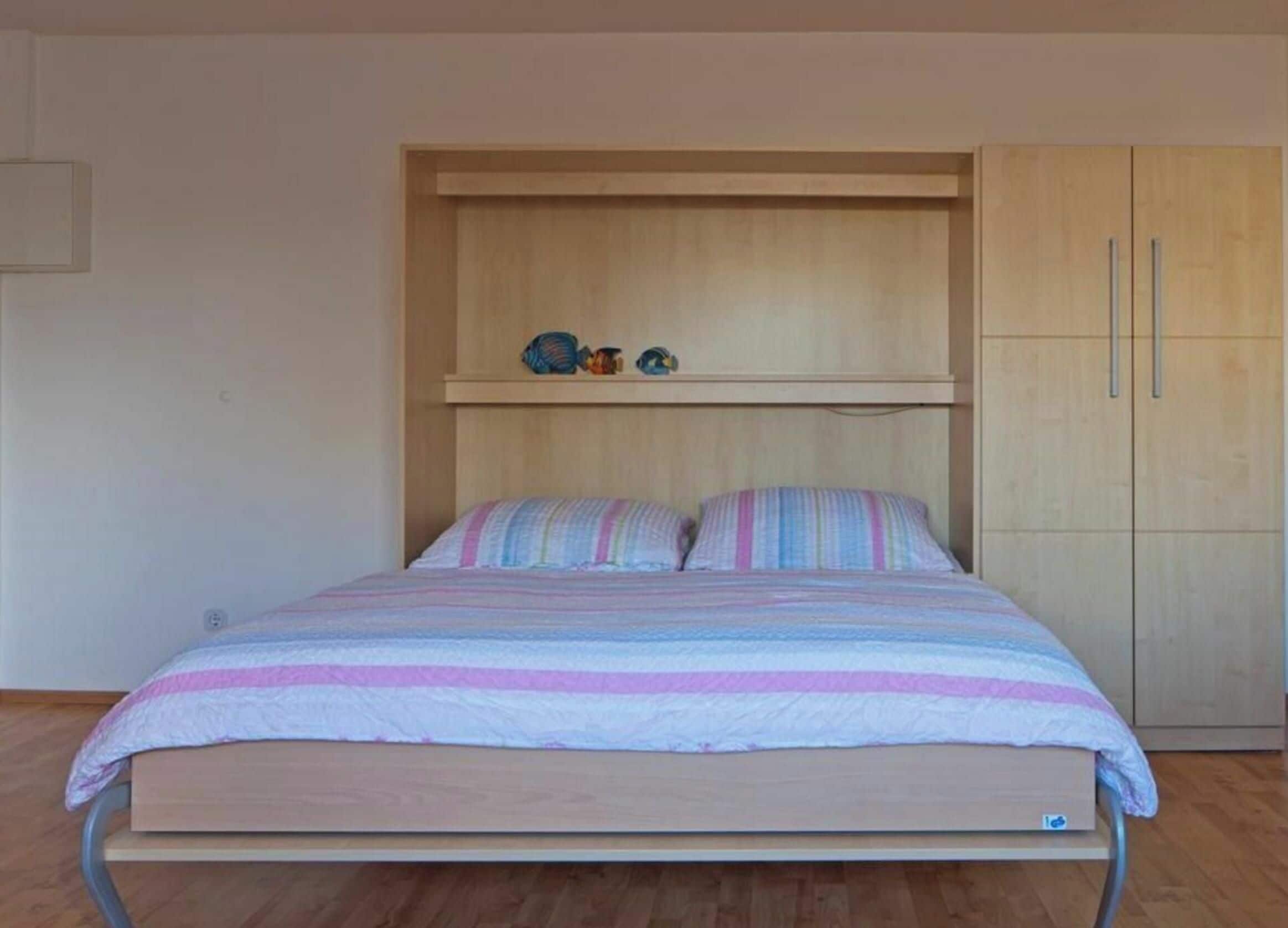Ein Einzelbett mit gestreifter Bettdecke, ein Holz-Kopfbrett und ein zweitüriger Holzschrank.