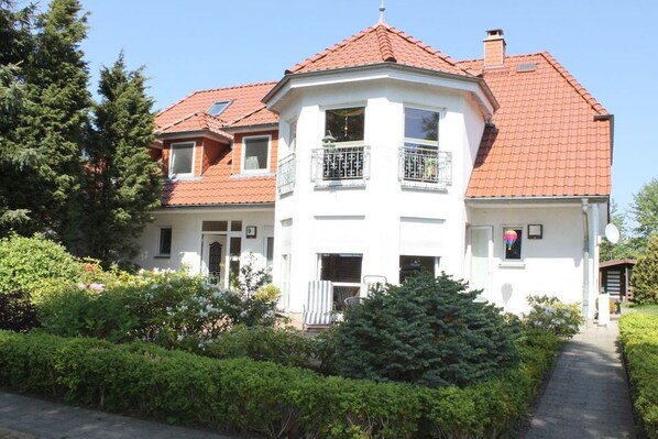 A two-story house with a red-tiled roof, a balcony with a metal railing, and a pathway leading to the entrance. - Holiday apartment with 4 bedrooms (Ostseeheilbad Zingst)