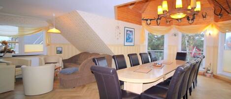 A dining area with a wooden table and chairs, a chandelier, and a staircase.