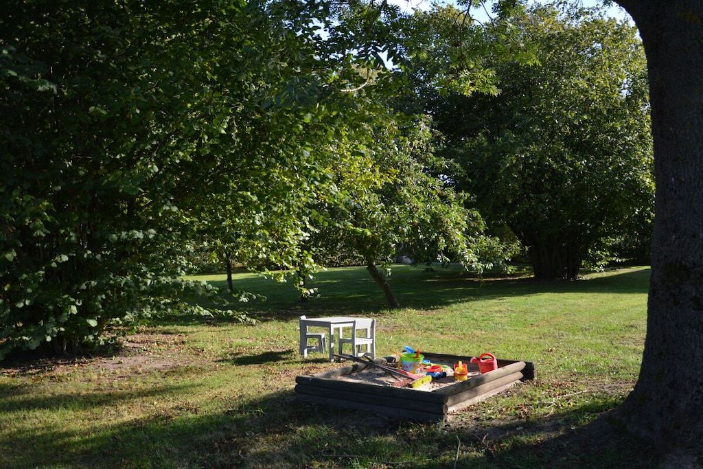 A wooden play structure with toys and a white chair in a grassy area with trees.