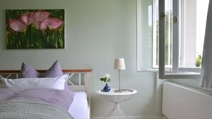 Quarto com cama, mesa de cabeceira com abajur, quadro na parede e janela.
