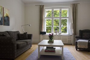 Ein Wohnzimmer mit einer Couch, einem Sessel, einem Couchtisch und einem Fenster mit Vorhängen.