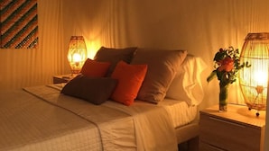A neatly made bed with pillows, a bedside table with a lamp, and a wall art piece. - Vrbo Property (Sainte Anne)
