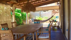 A wooden deck with a table and chairs, a hammock, and a view of greenery. - Vrbo Property (Sainte Anne)