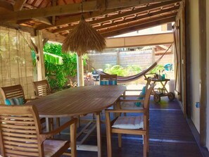 A wooden deck with a table and chairs, a hammock, and a view of greenery. - Vrbo Property (Sainte Anne)
