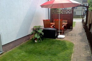 A patio area with a table and chairs, a potted plant, and a red umbrella. - Goodknecht Holiday Home (Rostock)