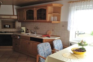 A kitchen with wooden cabinets, a sink, and a dining area with patterned chairs. - Goodknecht Holiday Home (Rostock)