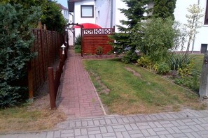 A paved pathway leading to a wooden gate, surrounded by greenery and a white building. - Goodknecht Holiday Home (Rostock)