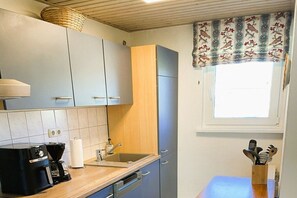 Une cuisine équipée d’une machine à café, d’un évier et d’une fenêtre agrémentée d’un rideau à motifs.