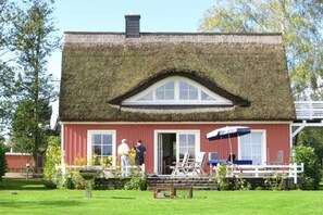 A red building with a thatched roof, a white porch, and a small garden area with outdoor furniture. - Holiday home in Pruchten with swimming pool (Pruchten)