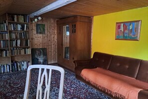 Ein Zimmer mit einem Holzbücherregal, einem braunen Sofa, einem gemusterten Teppich und einer gelben Wand.