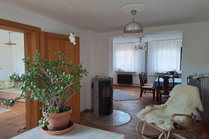 En stue med en stor potteplante, pejs, spiseområde med bord og stole, samt en hvid, blød lænestol.