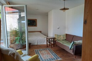 Et værelse med seng, sofa, et lille bord og en skydedør til et udendørs område med planter.
