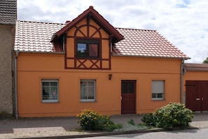 Ein zweistöckiges Gebäude mit rotem Ziegeldach, einem zentralen Fenster und einer Tür.