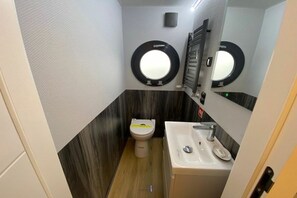 A compact bathroom with a toilet, sink, and two round mirrors. - Houseboat Fjord Vela (Barth)