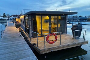 A modern floating structure with a dining area and a bar, connected to a dock. - Houseboat Fjord Vela (Barth)
