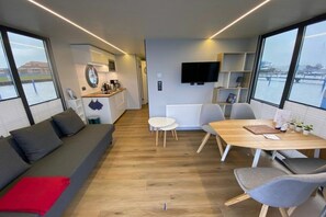 A modern interior with a sofa, dining table, chairs, a kitchen area, and large windows.