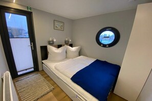 A bedroom with a bed, a window, a wall-mounted circular mirror, and a door. - Houseboat Fjord Vela (Barth)