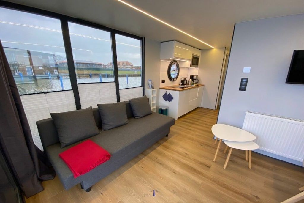 Sala moderna com sofá, mesinha de centro e vista para a água através de grandes janelas.