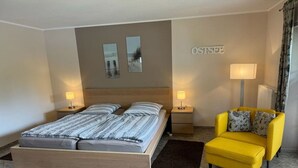 A bedroom with a double bed, two bedside tables with lamps, a yellow armchair, and a wall-mounted sign. - Holiday apartment Pahl (Ostseeheilbad Zingst)
