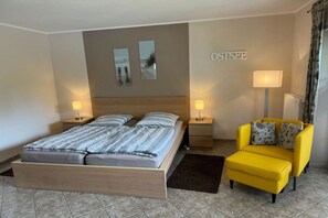 Een slaapkamer met een tweepersoonsbed, twee nachtkastjes met lampen, een gele fauteuil en een bord op de muur.