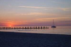 A sunset over a calm sea with a pier extending into the water and a sailboat anchored near the pier. - Holiday apartment Pahl (Ostseeheilbad Zingst)